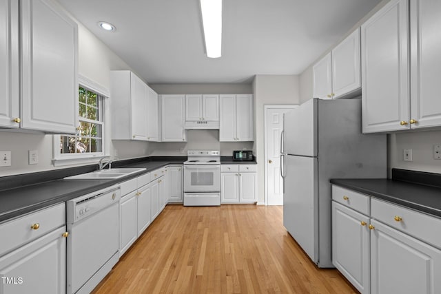 kitchen with dark countertops, a sink, white cabinets, under cabinet range hood, and white appliances