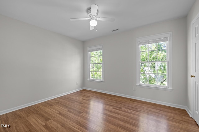 empty room with baseboards, ceiling fan, wood finished floors, and visible vents
