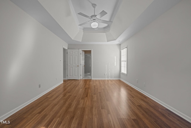unfurnished room featuring crown molding, wood finished floors, baseboards, ceiling fan, and a raised ceiling
