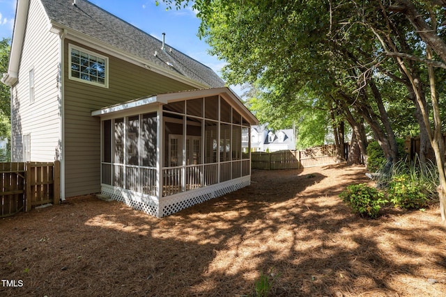 rear view of property featuring roof with shingles, a sunroom, and a fenced backyard