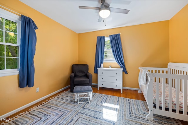 bedroom with baseboards, ceiling fan, wood finished floors, and a crib