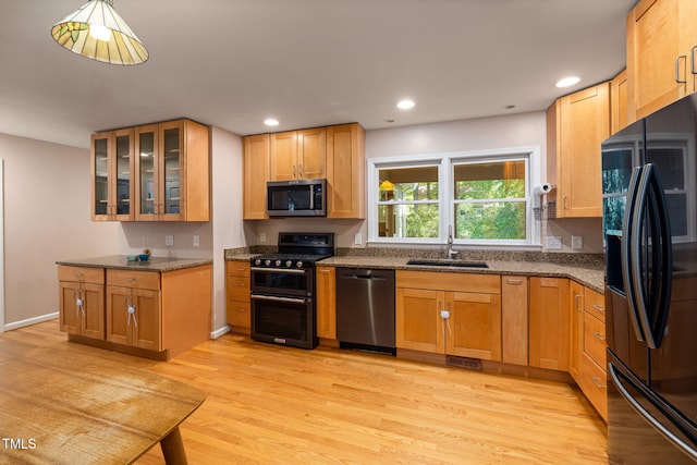 kitchen featuring glass insert cabinets, light wood-type flooring, dark stone counters, a sink, and black appliances