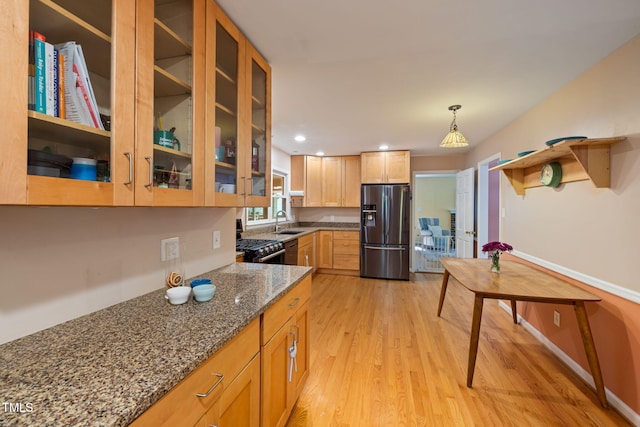 kitchen featuring range with gas stovetop, glass insert cabinets, stainless steel fridge, dark stone counters, and light wood-type flooring