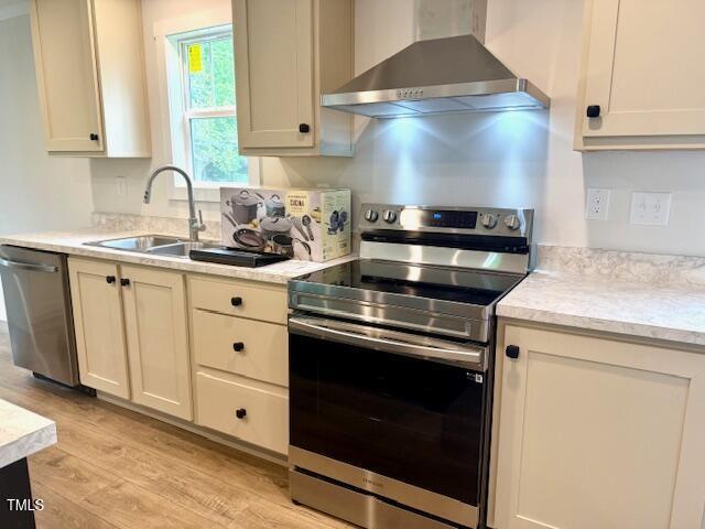 kitchen with appliances with stainless steel finishes, light wood-type flooring, light countertops, and wall chimney exhaust hood