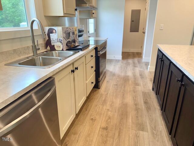 kitchen featuring a sink, appliances with stainless steel finishes, light countertops, electric panel, and light wood finished floors