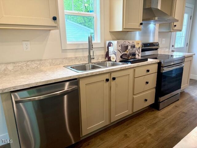 kitchen with stainless steel appliances, light countertops, wall chimney range hood, a sink, and dark wood-style floors