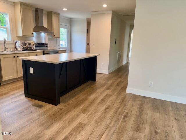 kitchen featuring wall chimney range hood, light countertops, baseboards, a center island, and electric range