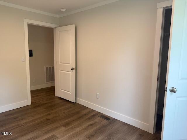 empty room with baseboards, visible vents, dark wood-style flooring, and crown molding