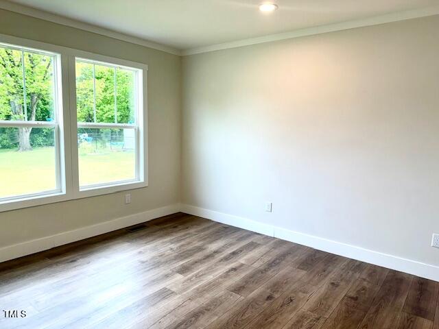 empty room with crown molding, wood finished floors, and baseboards