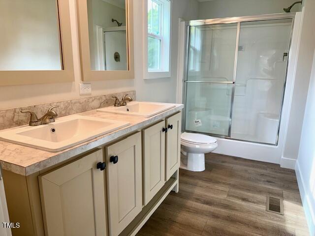 full bathroom featuring toilet, a sink, a shower with door, and visible vents
