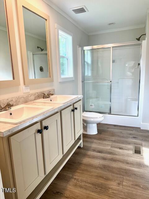 bathroom featuring ornamental molding, a sink, a shower with door, and visible vents