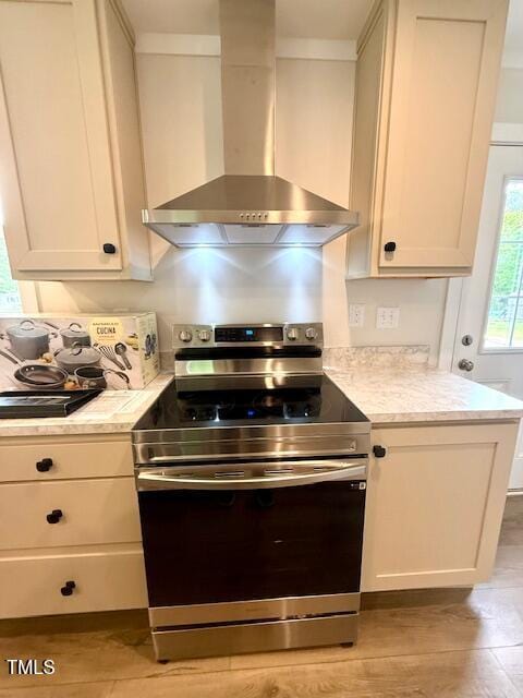 kitchen featuring electric range, light countertops, light wood-style flooring, and wall chimney exhaust hood