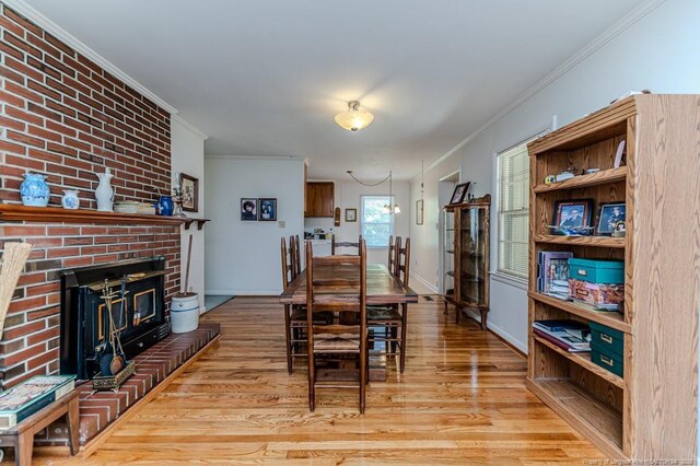 dining room featuring wood finished floors, ornamental molding, and a brick fireplace
