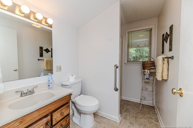 bathroom featuring baseboards, toilet, stone finish floor, and vanity
