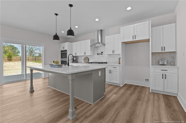 kitchen featuring white cabinets, light countertops, light wood finished floors, and wall chimney exhaust hood