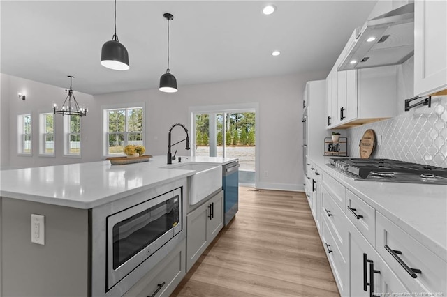 kitchen with wall chimney range hood, stainless steel appliances, light countertops, and a sink