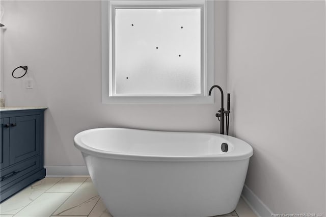 full bath featuring vanity, baseboards, marble finish floor, and a soaking tub