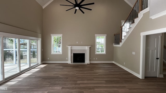 unfurnished living room featuring plenty of natural light, ceiling fan, high vaulted ceiling, and stairway