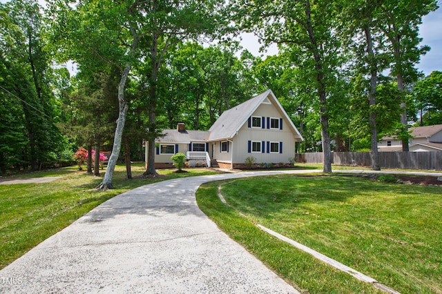 view of front of property featuring fence, a chimney, a front lawn, and curved driveway