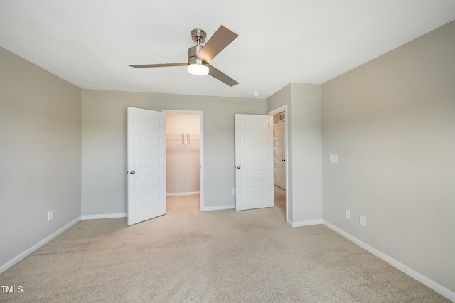 unfurnished bedroom featuring baseboards, ceiling fan, light carpet, and a spacious closet