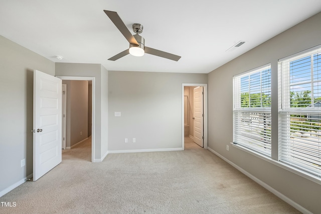 unfurnished bedroom with baseboards, ensuite bathroom, light carpet, and a ceiling fan