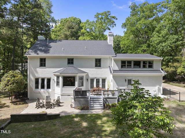 back of property with a chimney, a wooden deck, a fenced backyard, an outdoor fire pit, and a patio