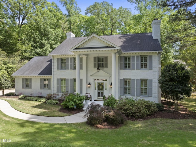 view of front of house featuring roof with shingles, a chimney, and a front yard