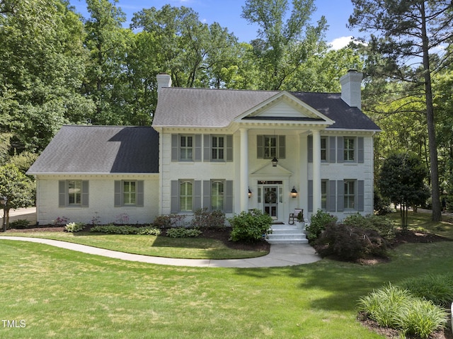 neoclassical / greek revival house featuring a chimney, a shingled roof, and a front lawn
