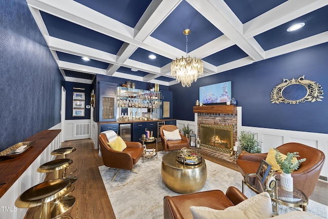 living area with coffered ceiling, beam ceiling, wood finished floors, a bar, and a decorative wall