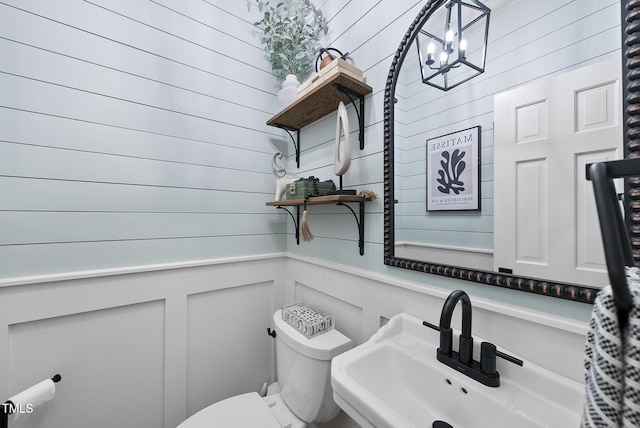 half bathroom featuring a sink, a decorative wall, toilet, and a notable chandelier