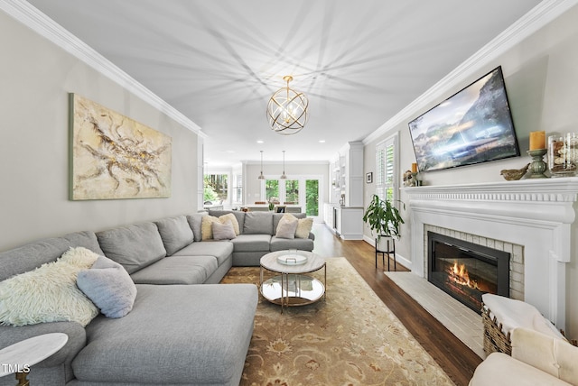 living area with ornamental molding, a glass covered fireplace, wood finished floors, and a chandelier