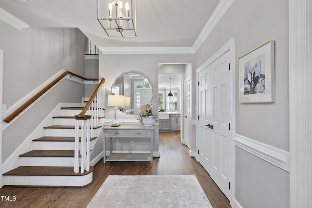 entryway with an inviting chandelier, ornamental molding, dark wood-style floors, and stairway