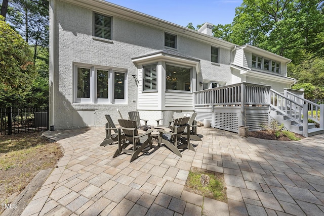rear view of house with fence, a deck, stucco siding, a chimney, and a patio area