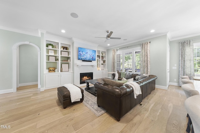 living area featuring ornamental molding, a fireplace, baseboards, light wood-style floors, and a ceiling fan