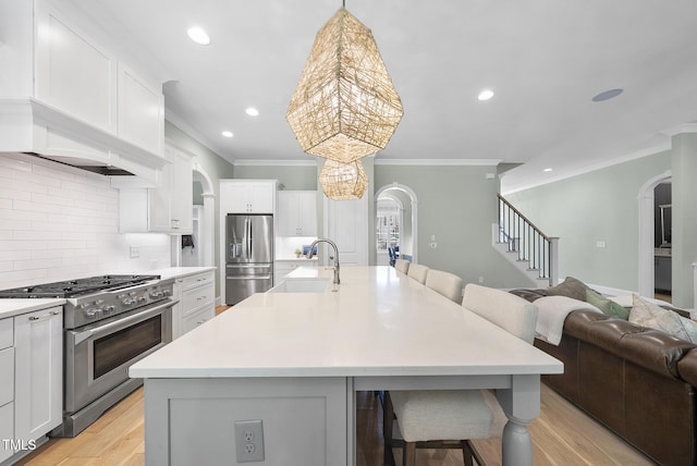 kitchen featuring appliances with stainless steel finishes, a sink, arched walkways, open floor plan, and ornamental molding