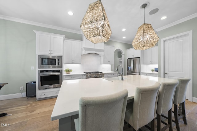 kitchen featuring crown molding, arched walkways, white cabinets, a sink, and appliances with stainless steel finishes