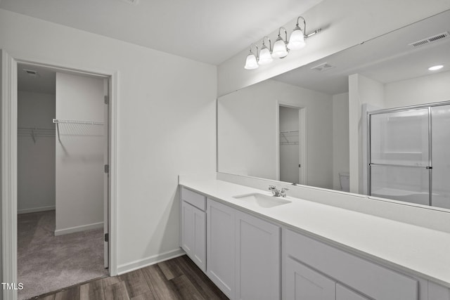 bathroom with wood finished floors, a shower with door, baseboards, vanity, and a walk in closet