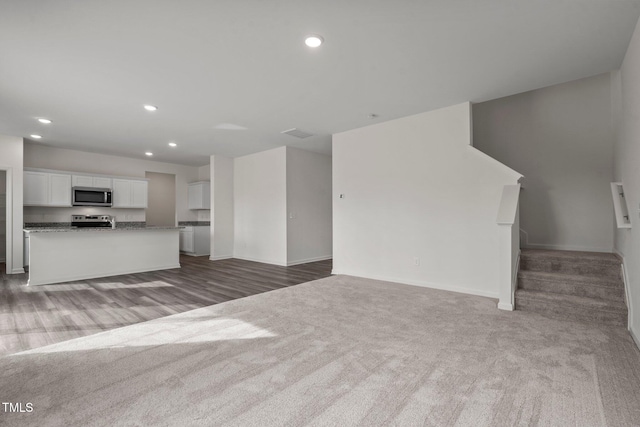 unfurnished living room featuring carpet, recessed lighting, baseboards, stairway, and wood finished floors