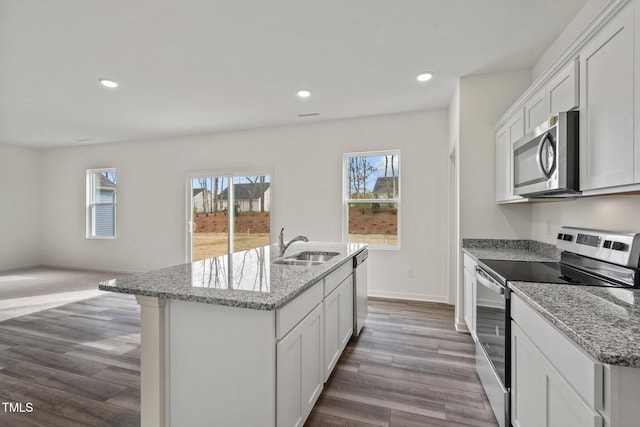 kitchen with stainless steel appliances, a sink, an island with sink, dark wood-type flooring, and light stone countertops