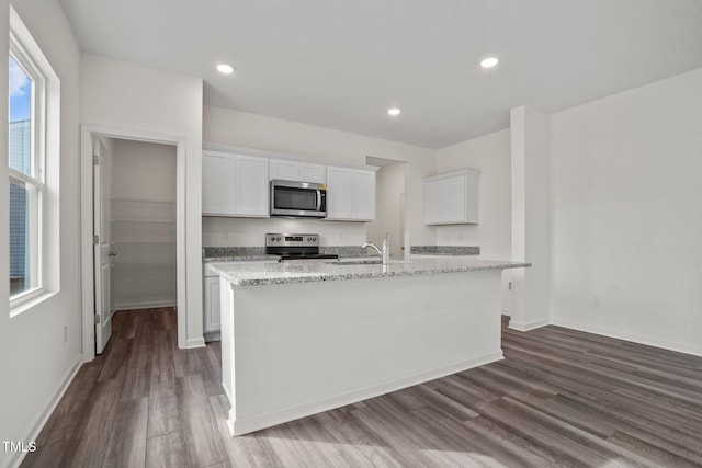 kitchen with appliances with stainless steel finishes, dark wood-style flooring, white cabinets, a kitchen island with sink, and light stone counters