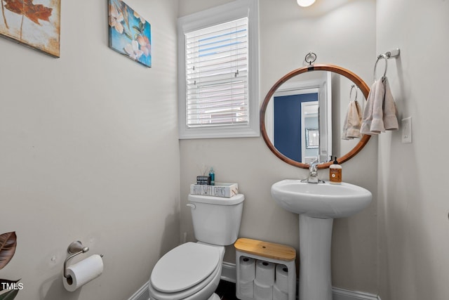 half bath with baseboards, toilet, and a sink
