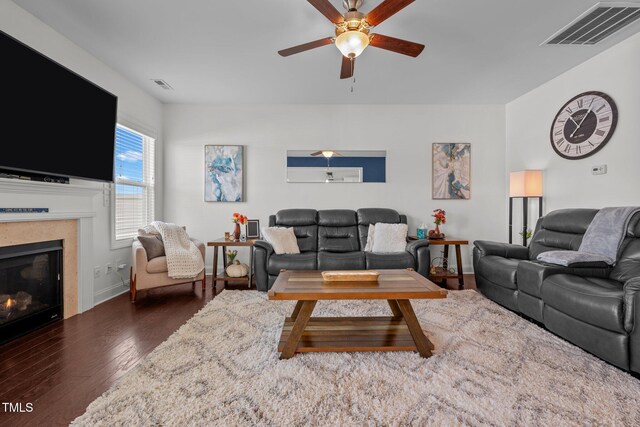 living area with visible vents, ceiling fan, wood finished floors, and a warm lit fireplace