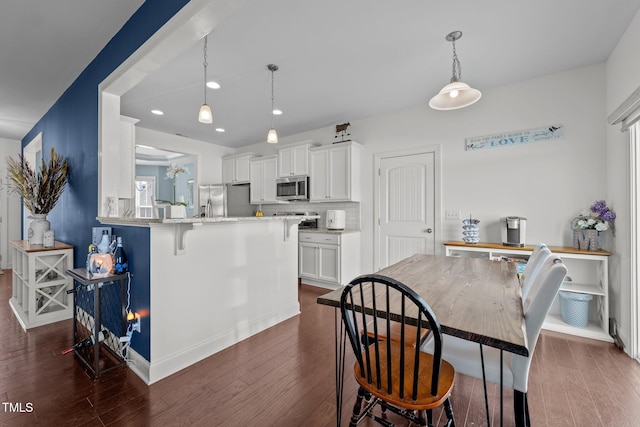 kitchen featuring a kitchen breakfast bar, white cabinetry, stainless steel appliances, recessed lighting, and dark wood-type flooring