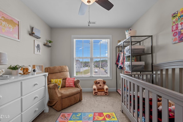 bedroom with visible vents, baseboards, a crib, light carpet, and a ceiling fan