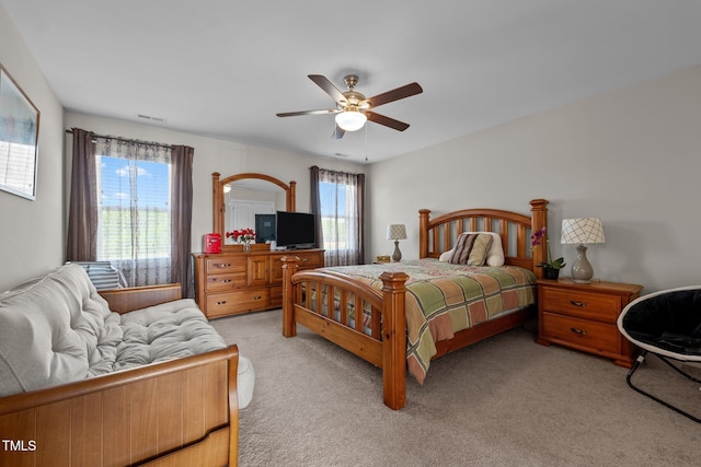 bedroom with light colored carpet, visible vents, ceiling fan, and multiple windows