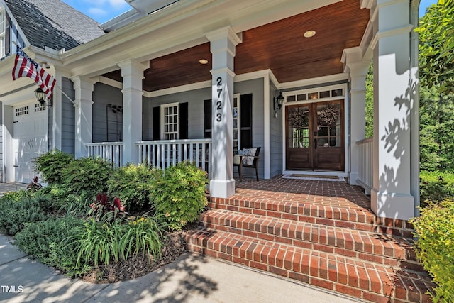 doorway to property with a porch, an attached garage, and a shingled roof