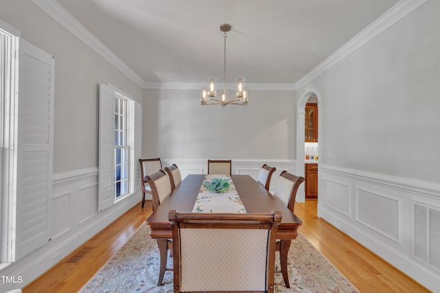 dining space with an inviting chandelier, ornamental molding, and light wood-style flooring
