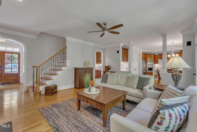 living area with arched walkways, a ceiling fan, ornamental molding, and light wood-type flooring
