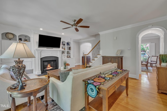 living area with crown molding, arched walkways, ceiling fan, and light wood-type flooring