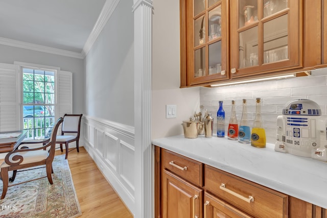 bar featuring crown molding, light wood finished floors, a decorative wall, a wainscoted wall, and tasteful backsplash